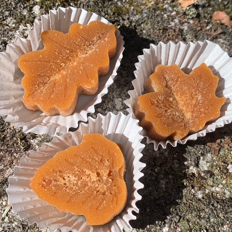 May include: Three maple leaf shaped candies in white paper cups. The candies are a light brown color and have a slightly grainy texture.