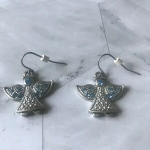 May include: A pair of silver angel earrings with blue crystal accents. The earrings have a hook closure.