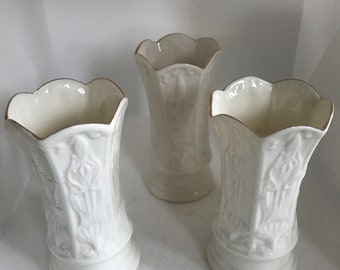 Könnte beinhalten: Drei weiße Keramikvasen mit gewelltem Rand und goldenem Besatz. Die Vasen haben ein strukturiertes, geprägtes Design und einen Sockel. Die Vasen sind auf einer weißen Oberfläche angeordnet.