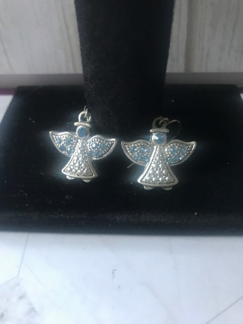 May include: A pair of silver angel earrings with blue crystal accents.