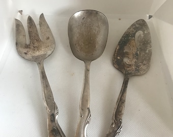 Könnte beinhalten: Drei silberne Servierbesteck, eine Gabel, ein Löffel und ein Serviermesser mit verzierten Griffen.