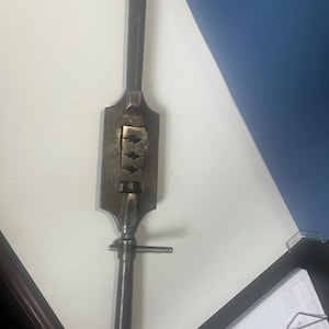 May include: A vintage metal tool with a long handle and a rectangular head. The head has a series of small, rectangular openings. A smaller handle is attached to the main body with a screw. The tool is made of dark metal and appears to be well-used.