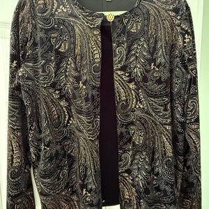 May include: A black and gold paisley print jacket with a single gold button closure. The jacket has long sleeves and is hanging on a green hanger. The brand name "notations" is visible on the back of the collar.