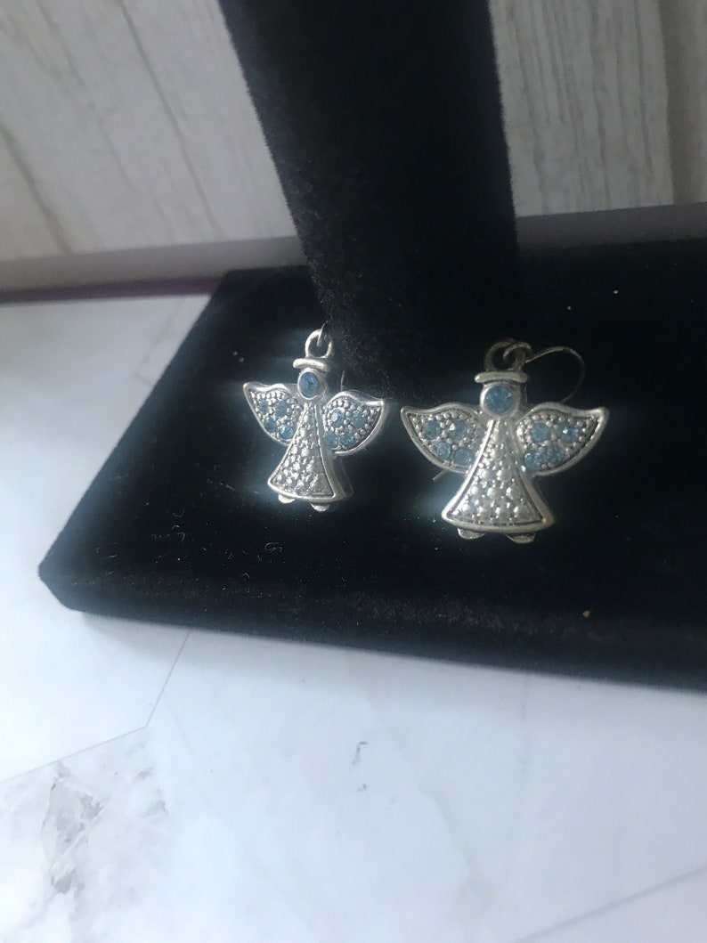 May include: A pair of silver angel earrings with blue crystal accents.