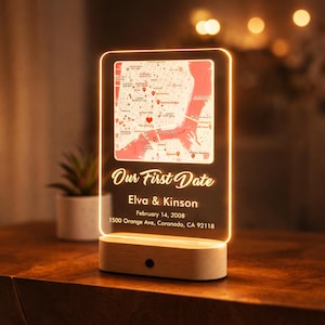 May include: A personalized LED night light with a map design. The light features a map with a heart marking a location, the text "Our First Date", names, date, and address. The base is made of wood.