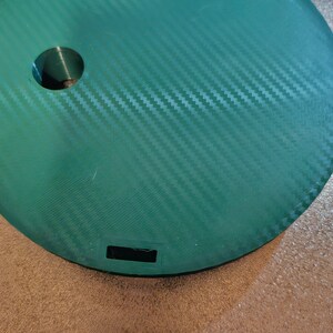 May include: A green circular platform with a textured surface and a small hole in the center. The platform has two rectangular cutouts on the edge.