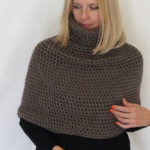 May include: A brown, open-weave crochet poncho with a turtleneck collar. The poncho is a solid color and appears to be handmade. The garment is worn over a black top.
