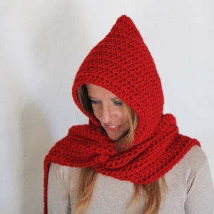 May include: A red crocheted hooded scarf with a long scarf attached. The scarf is worn by a person with long blonde hair.