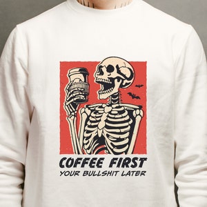 SVG PNG illustration of a skeleton holding a coffee cup with the humorous text Coffee first, Your bullshit later, designed in a playful style to celebrate Halloween. This quirky design combines a love for coffee with a cheeky message.