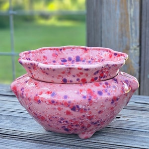 May include: A pink and purple speckled ceramic planter with a scalloped top rim. The planter has a double layer design with a smaller top planter and a larger bottom planter.
