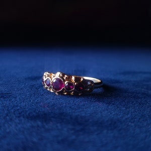 Op de afbeelding: Een gouden ring met drie robijnrode edelstenen gezet in een decoratieve band.