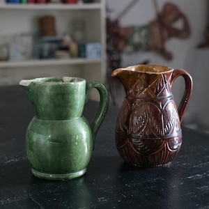 Pode incluir: Dois jarros de cerâmica, um verde e outro marrom com um padrão de folhas.