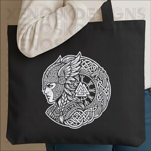 Op de afbeelding: Zwarte draagtas met een witte afbeelding van een Viking-krijger in profiel, versierd met een gevleugelde helm en ingewikkeld knoopwerk. Het ontwerp bevat runen en een cirkelvormige rand, wat een gedurfde, gedetailleerde esthetiek cre&euml;ert.