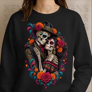 May include: A black crewneck sweatshirt featuring a vibrant graphic of two skeletons embracing. The skeletons are dressed in formal attire with intricate floral patterns, colourful marigolds, and roses in shades of red, orange, and teal.