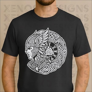 Op de afbeelding: Zwart t-shirt met een witte afbeelding van een Vikingvrouw in profiel, met een gevleugelde helm en ingewikkeld knoopwerk. Het ontwerp bevat runen en een driehoekig symbool. Het shirt heeft een ronde hals en korte mouwen.