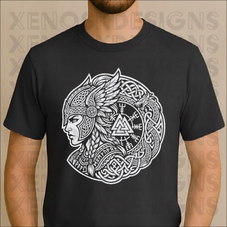 Op de afbeelding: Zwart t-shirt met een witte afbeelding van een Vikingvrouw in profiel, met een gevleugelde helm en ingewikkeld knoopwerk. Het ontwerp bevat runen en een driehoekig symbool. Het shirt heeft een ronde hals en korte mouwen.