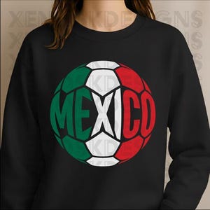 May include: A black long-sleeve sweatshirt featuring a large graphic of a soccer ball on the chest. The ball is colored in green, white, and red, representing the Mexican flag, with the word MEXICO printed in bold letters across the center.