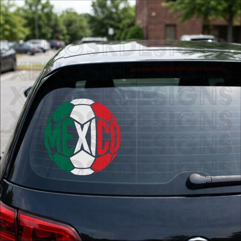 May include: A circular decal applied to the rear window of a black vehicle. The decal features a soccer ball design colored in green, white, and red, representing the Mexican flag, with the word MEXICO integrated into the ball's pattern.