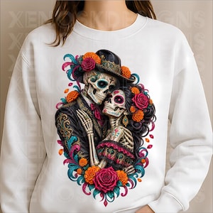 May include: A white long-sleeve sweatshirt featuring a central graphic of two skeletons embracing. The skeletons are adorned with colourful floral patterns, wearing a black hat and dark clothing, surrounded by vibrant orange and pink roses.