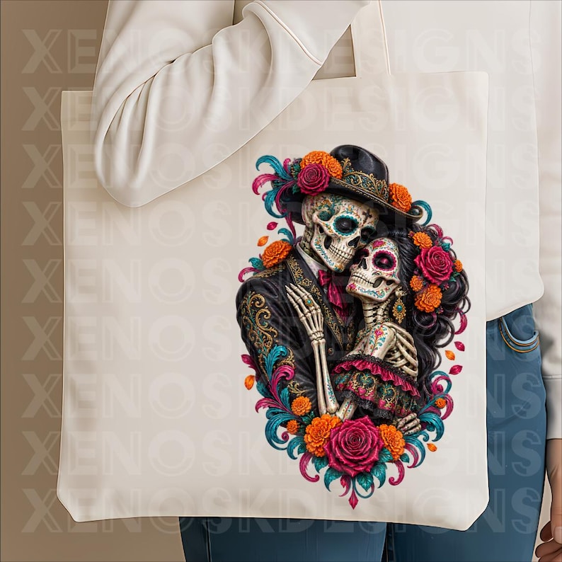 May include: A cream-coloured tote bag featuring a vibrant graphic of two skeletons embracing. The skeletons are adorned with colourful floral accents, including orange marigolds and deep pink roses, with intricate patterns on their clothing.