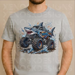 May include: A light grey t-shirt with a shark-themed monster truck design. The truck is blue and white, with the text "The Shark Monster Truck". The image includes water splashes and lightning bolts.