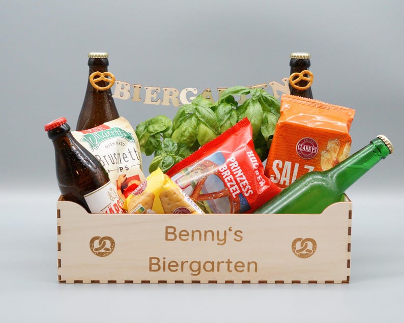 Puede incluir: Una caja de madera con las palabras "Benny's Biergarten" grabadas en la parte delantera. La caja est&aacute; llena de varios bocadillos y bebidas, incluyendo pretzels, patatas fritas y cerveza.