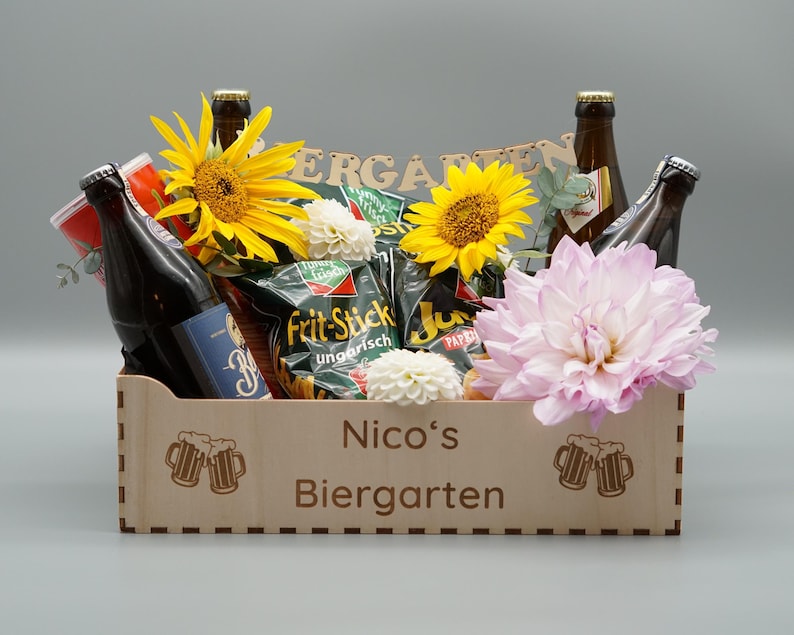 Puede incluir: Una caja de madera llena de cerveza, patatas fritas y flores. La caja est&aacute; grabada con "Nico's Biergarten".