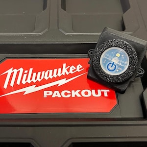 May include: A black Milwaukee Packout toolbox with a white logo and a small black and blue LED light with a power button.
