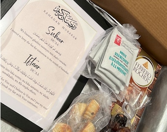 May include: A gift box filled with Ramadan treats. The box contains a framed print with Arabic text, a bag of dates, a bag of cookies, and a box of chocolate. The print reads "Ramadan Mubarak" and includes Arabic text for "Suhoor Du'aa" and "Iftaar Du'aa".