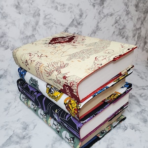 May include: A stack of four books with colourful covers featuring Harry Potter themed designs. The top book has a red and white cover with a map of Hogwarts and the text "The Marauder's Map".