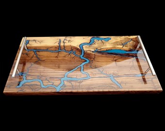 May include: A rectangular wooden serving tray with a unique design. The tray features a natural wood grain pattern with blue resin accents resembling a river or lightning. It has silver metal handles on each end.