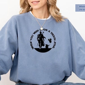 May include: A blue sweatshirt with a black graphic print of a character from the Star Wars franchise. The graphic features the text "When you wish upon a death star".