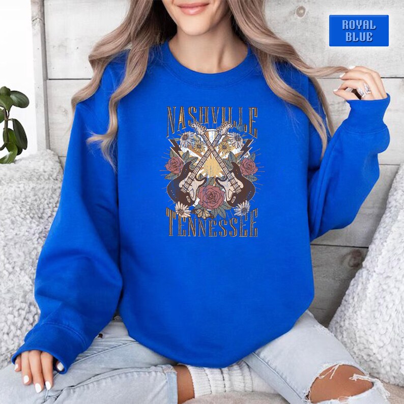 May include: A royal blue sweatshirt with a graphic design featuring two crossed guitars with floral accents. The text "Nashville Tennessee" is printed below the guitars.