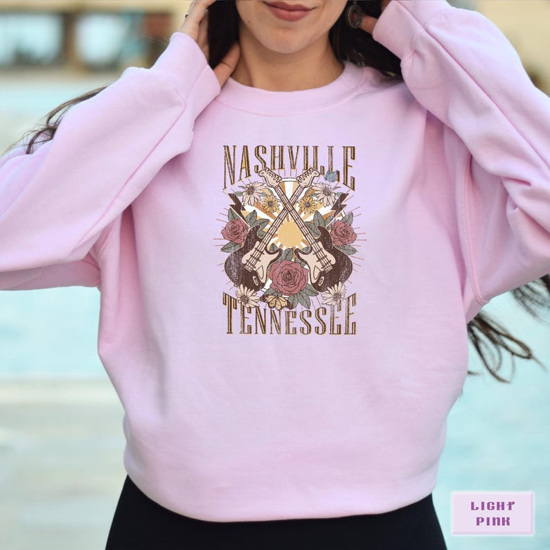 May include: Light pink sweatshirt with a graphic design of two guitars crossed over each other with flowers and the text "Nashville Tennessee".