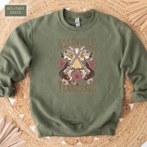 May include: A green sweatshirt with a graphic print of two guitars crossed over each other with flowers and the text "Nashville Tennessee".