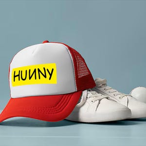 May include: A red and white trucker hat with the word "HUUNY" in black letters on a yellow rectangle. White sneakers and a baseball are next to the hat.