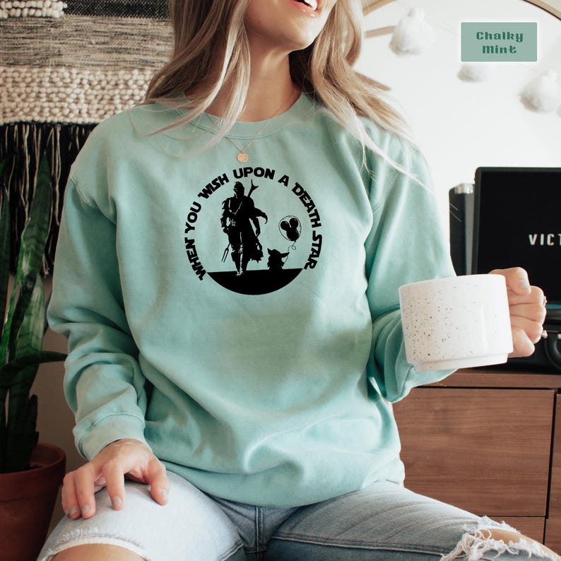 May include: A light blue sweatshirt with a black graphic print of a character from the Star Wars franchise. The graphic includes the text "When you wish upon a death star".