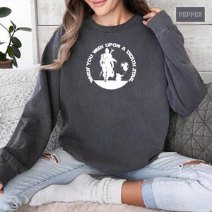 May include: A dark gray sweatshirt with a white circle graphic featuring a silhouette of a person and a small creature. The text around the graphic reads "When you wish upon a death star."
