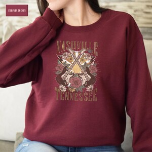 May include: A maroon sweatshirt with a graphic print of two guitars crossed over each other with flowers and the text "Nashville Tennessee".