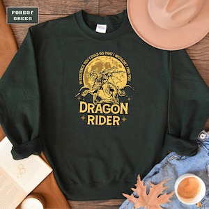 May include: A dark green sweatshirt with a yellow graphic of a dragon riding a knight. The graphic is surrounded by a yellow circle with the text "In existence you could go that I wouldn't find you" and the text "Dragon Rider" below the graphic.
