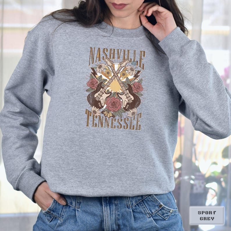 May include: A gray sweatshirt with a vintage-style graphic design featuring two guitars crossed over each other with flowers and the text "Nashville Tennessee".