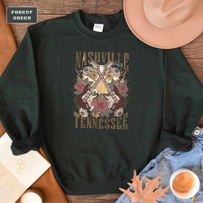 May include: A dark green sweatshirt with a graphic print of two guitars crossed over each other with flowers and the text "Nashville Tennessee".