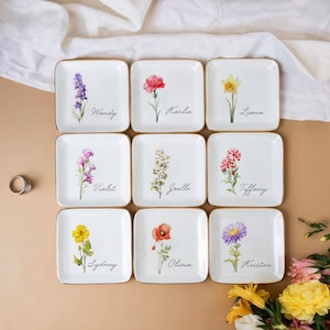 May include: Nine white ceramic ring dishes with gold trim, each featuring a different floral design and a name. The names are Wendy, Karlie, Liana, Violet, Joelle, Tiffany, Sydney, Olivia, and Kristen.