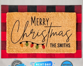 Könnte beinhalten: Eine braune Kokosnuss-Fußmatte mit dem Text "Merry Christmas" in schwarzer Kursivschrift mit einer Lichterkette darunter. Der Text "The Smiths" steht ebenfalls in schwarzer Schrift unter den Lichtern.