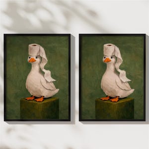 May include: Two identical framed wall art prints featuring a white duck with an orange beak and feet standing on a dark green block. The duck has a roll of white toilet paper balanced on its head with a single sheet draped down its side.