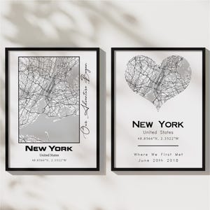 May include: Two black framed prints with a map of New York City. The first print shows the city in a standard map format with the text "Our Adventure Began" written vertically on the right side. The second print shows the city in the shape of a heart with the text "NEW YORK, United States, 48.8566°N, 2.3522°W, Where We First Met, June 20th 2018".