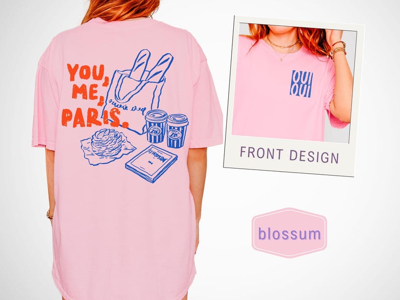 May include: Pink t-shirt with a graphic on the back featuring the words "YOU, ME, PARIS" in red and blue, along with illustrations of a baguette, coffee cups, and a pastry. A smaller image shows the front design with the text "OUI OUI".