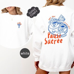May include: White sweatshirt with a floral design on the front and a French-themed graphic on the back. The back graphic includes a croissant, coffee, and the words "Pause Sucrée" in orange and blue.