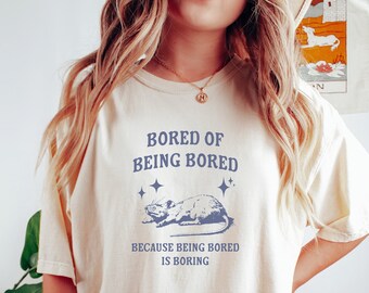 May include: A white t-shirt with the text "Bored of being bored. Because being bored is boring." and a cartoon rat with stars above it.
