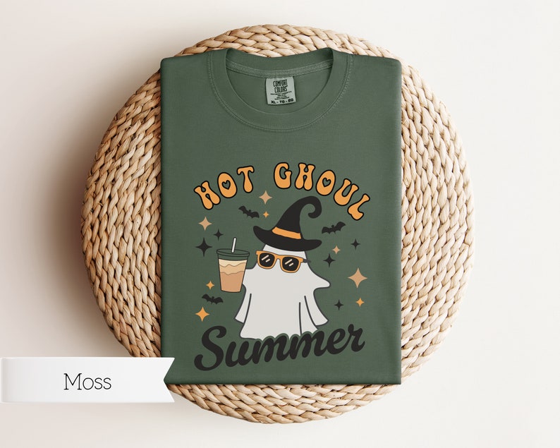 May include: A green t-shirt with a ghost wearing sunglasses and a witch hat holding a cup of coffee. The text on the shirt reads "Hot Ghoul Summer".